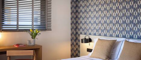 A bedroom with a bed, a desk, a lamp, and a patterned wall.