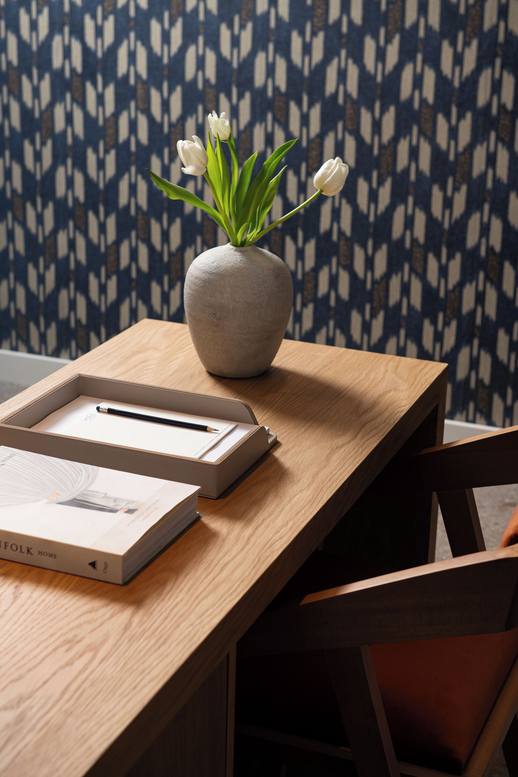 Una mesa de madera con un jarrón de tulipanes blancos, un cuaderno y un bolígrafo.