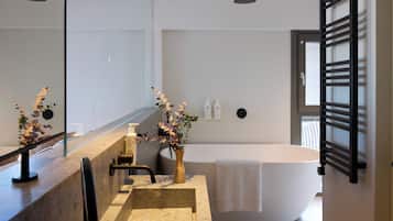 A modern bathroom with a large bathtub, a vanity with a mirror, and a vase with flowers.