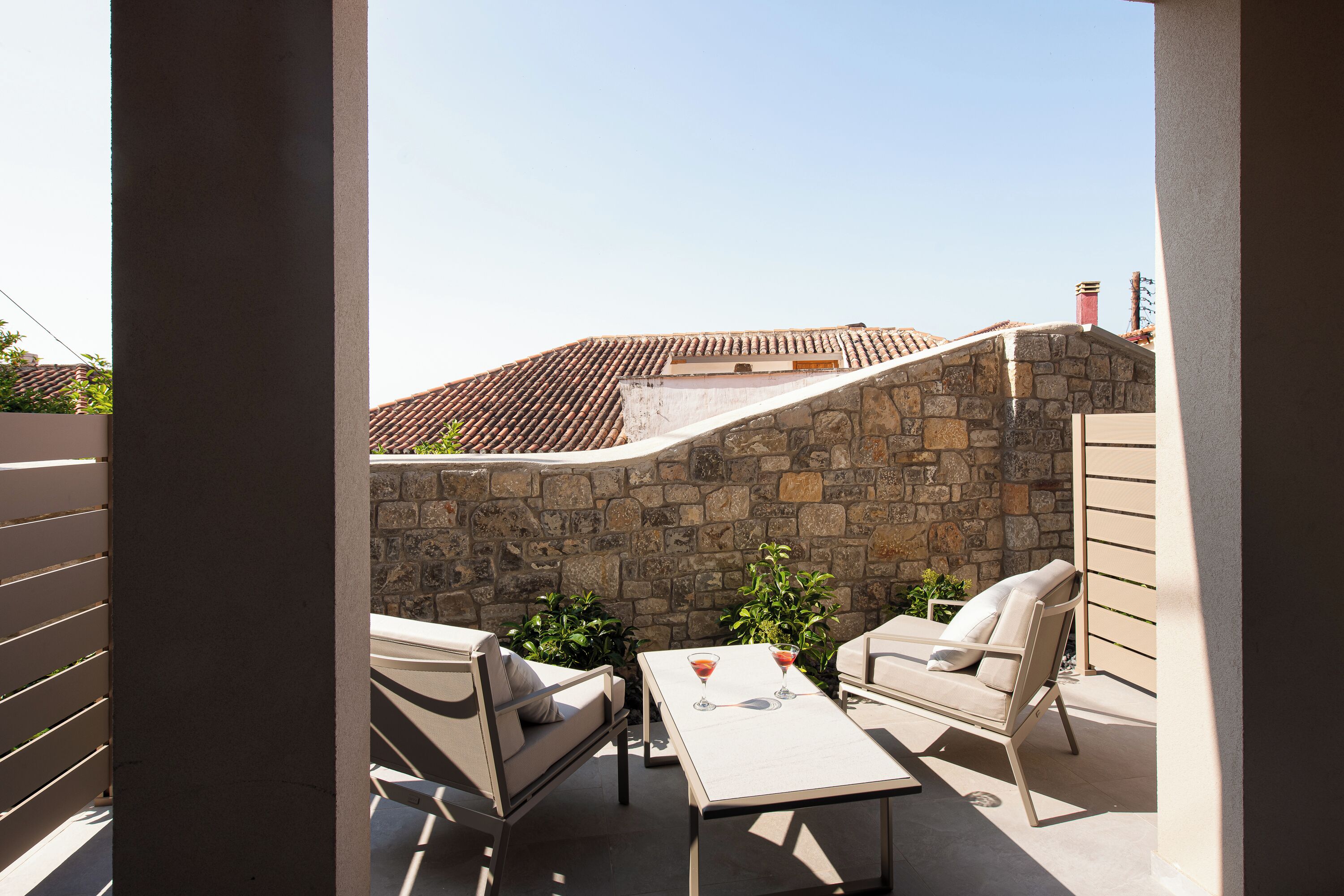 Un patio con un muro de piedra, dos sillones, una mesa y dos copas de martini.