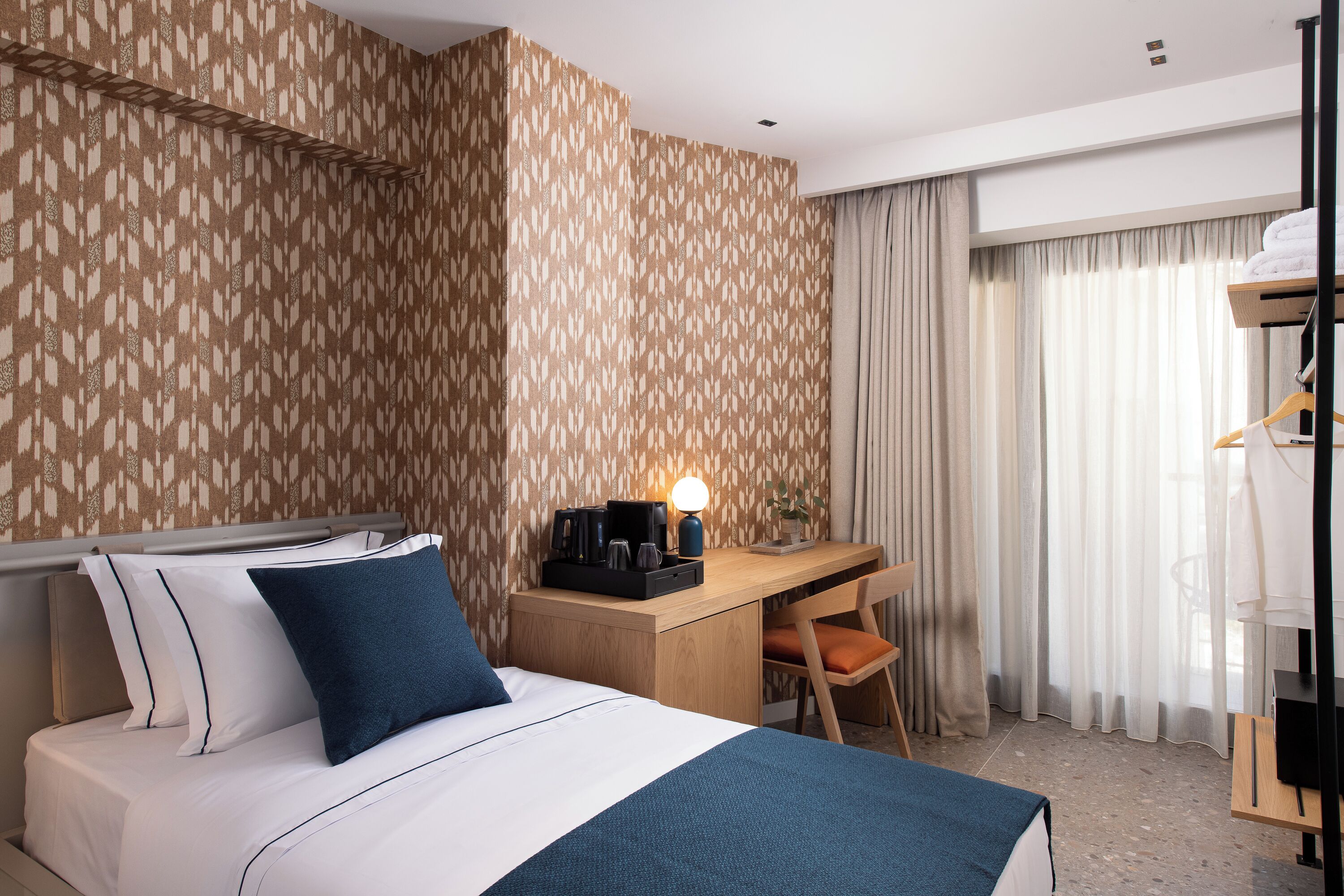 A hotel room with a bed, a desk, a chair, a wardrobe, and a window with curtains.