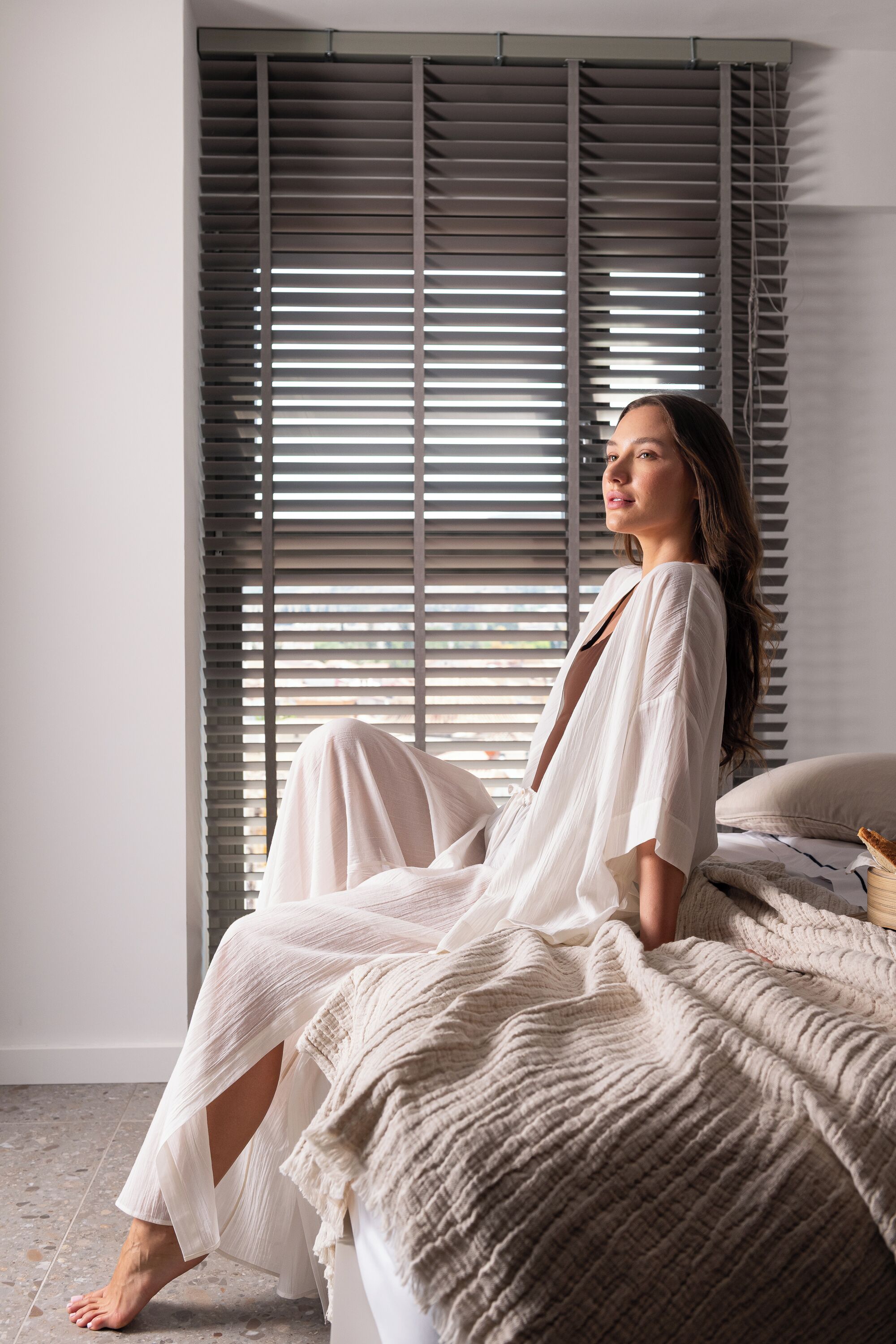 A person sitting on a bed with a window in the background.