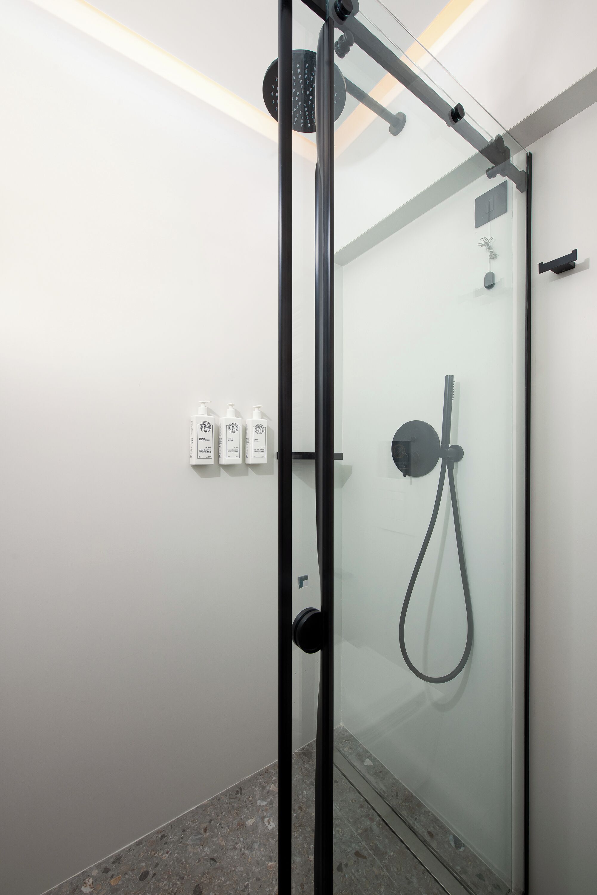 Ducha moderna con cabina de vidrio, cabezal de ducha de mano y panel de control en la pared.