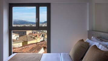 A hotel room with a large window offering a cityscape view, a neatly made bed, and a headboard with a textured design.