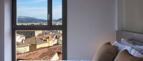 A hotel room with a large window offering a cityscape view, a neatly made bed, and a headboard with a textured design.