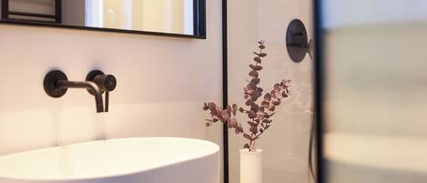 A modern bathroom with a large white sink, a mirror, and a small vase with dried flowers.