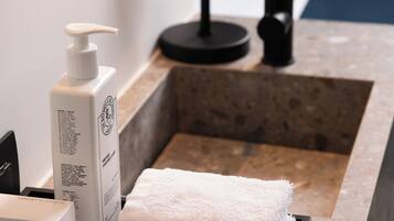 Un baño con lavamanos, espejo, jabón para manos y toalla.
