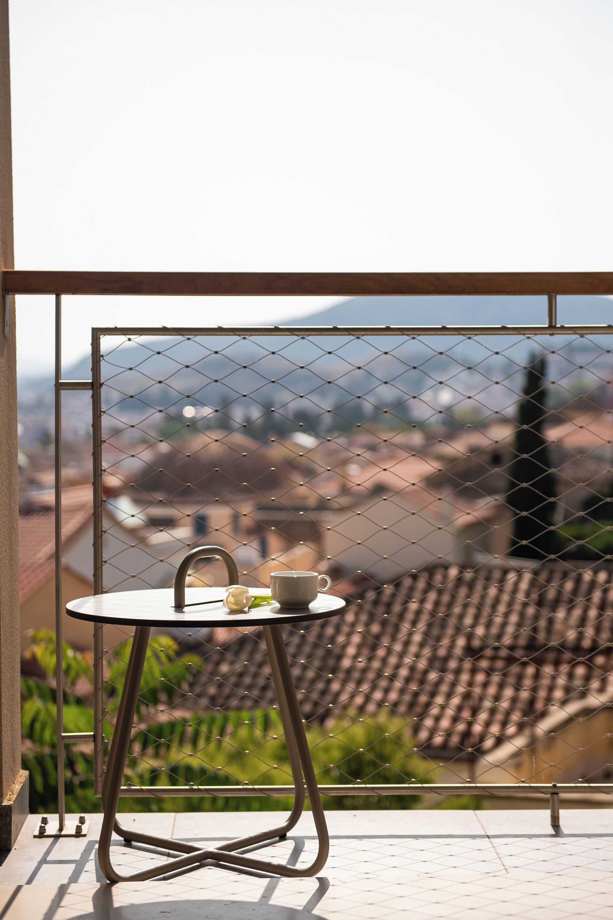A balcony with a table and chairs, a view of buildings and greenery, and a metal fence.