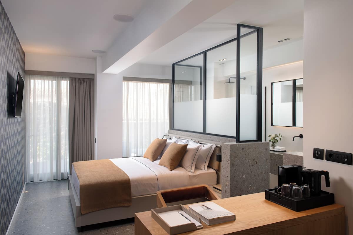 A modern hotel room with a large bed, a wooden desk, a coffee maker, and a mirror.