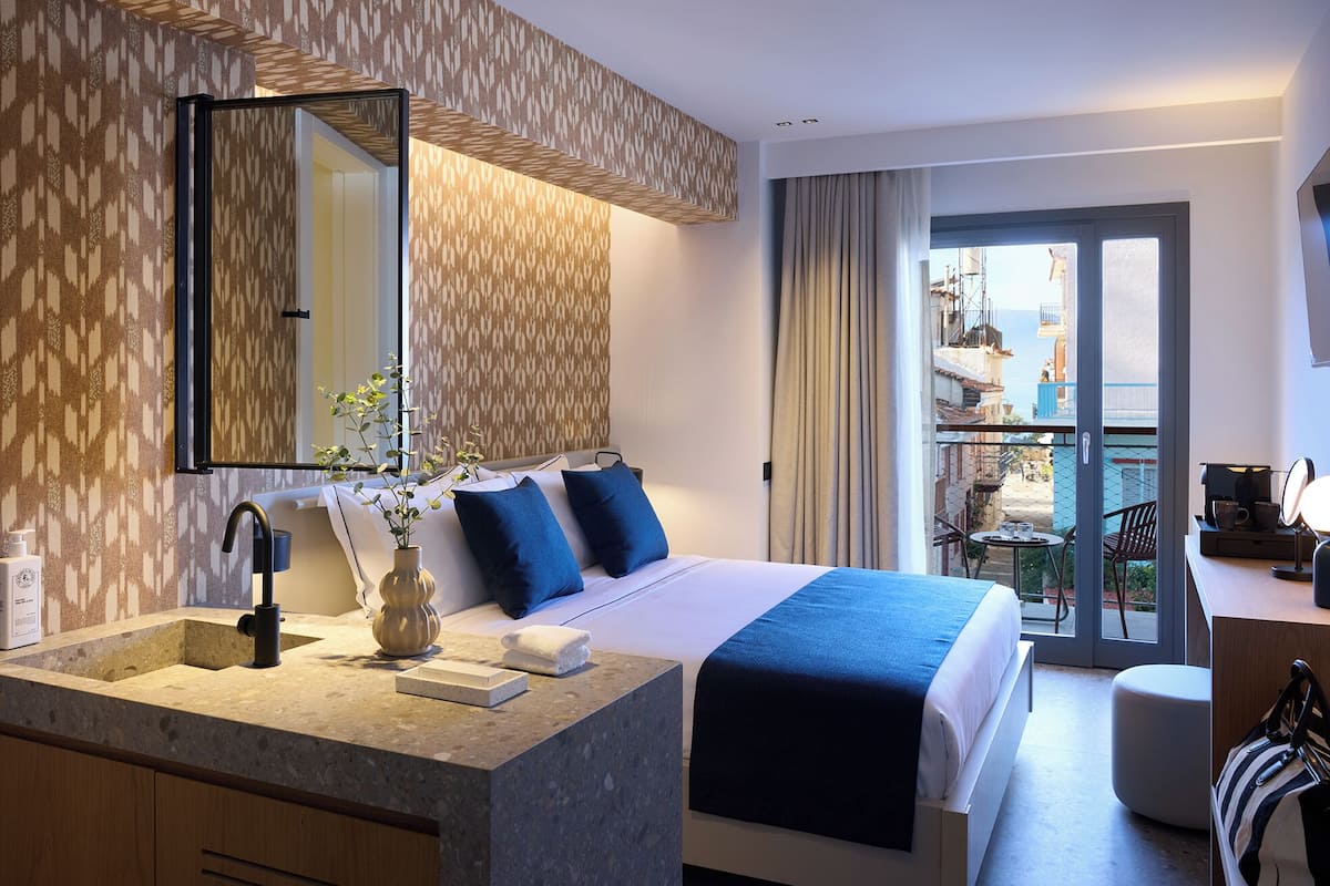 A hotel room with a bed, a bathroom with a sink, a mirror, and a view of the outside balcony.