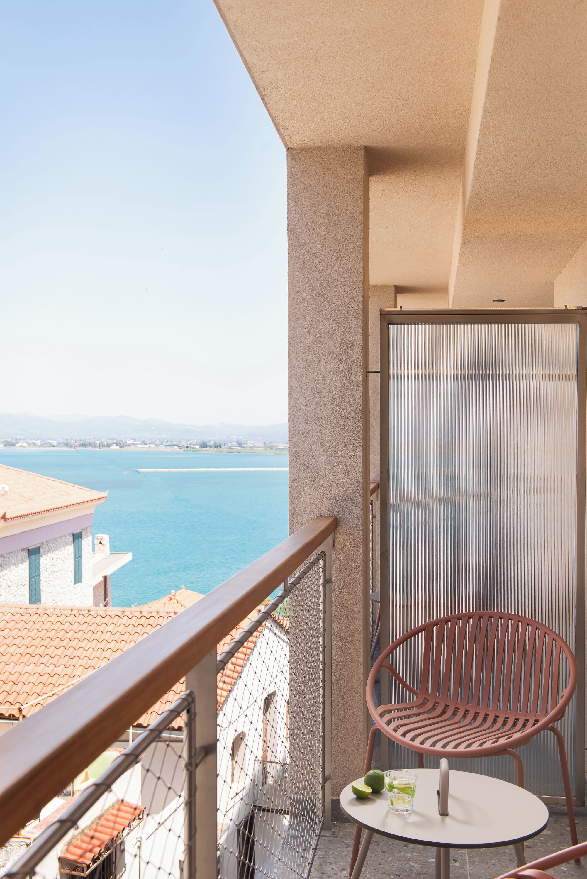 A balcony with a view of the sea, a chair, and a table with a glass and lime.