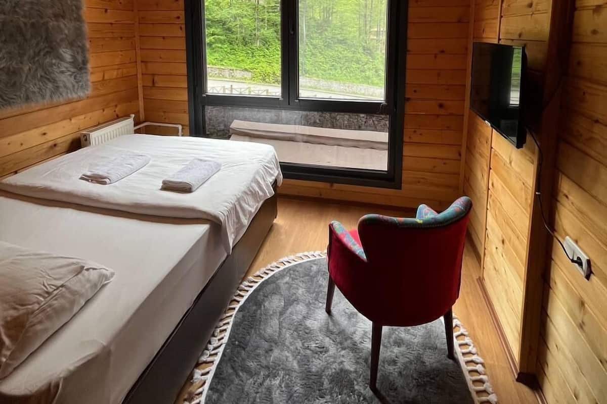 A wooden cabin bedroom with a bed, a chair, a window, and a ceiling light.
