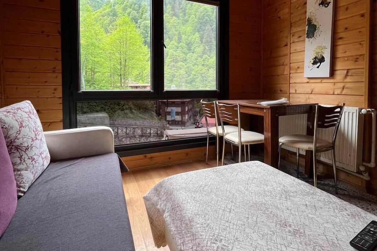 A cozy cabin room with a bed, a desk, and a window overlooking a forest.
