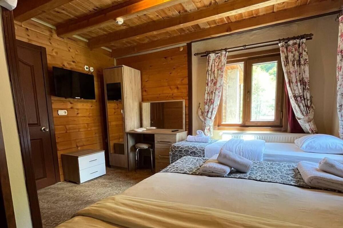 A cozy bedroom with a wooden ceiling, a bed with white linens, a desk with a chair, and a television on the wall.