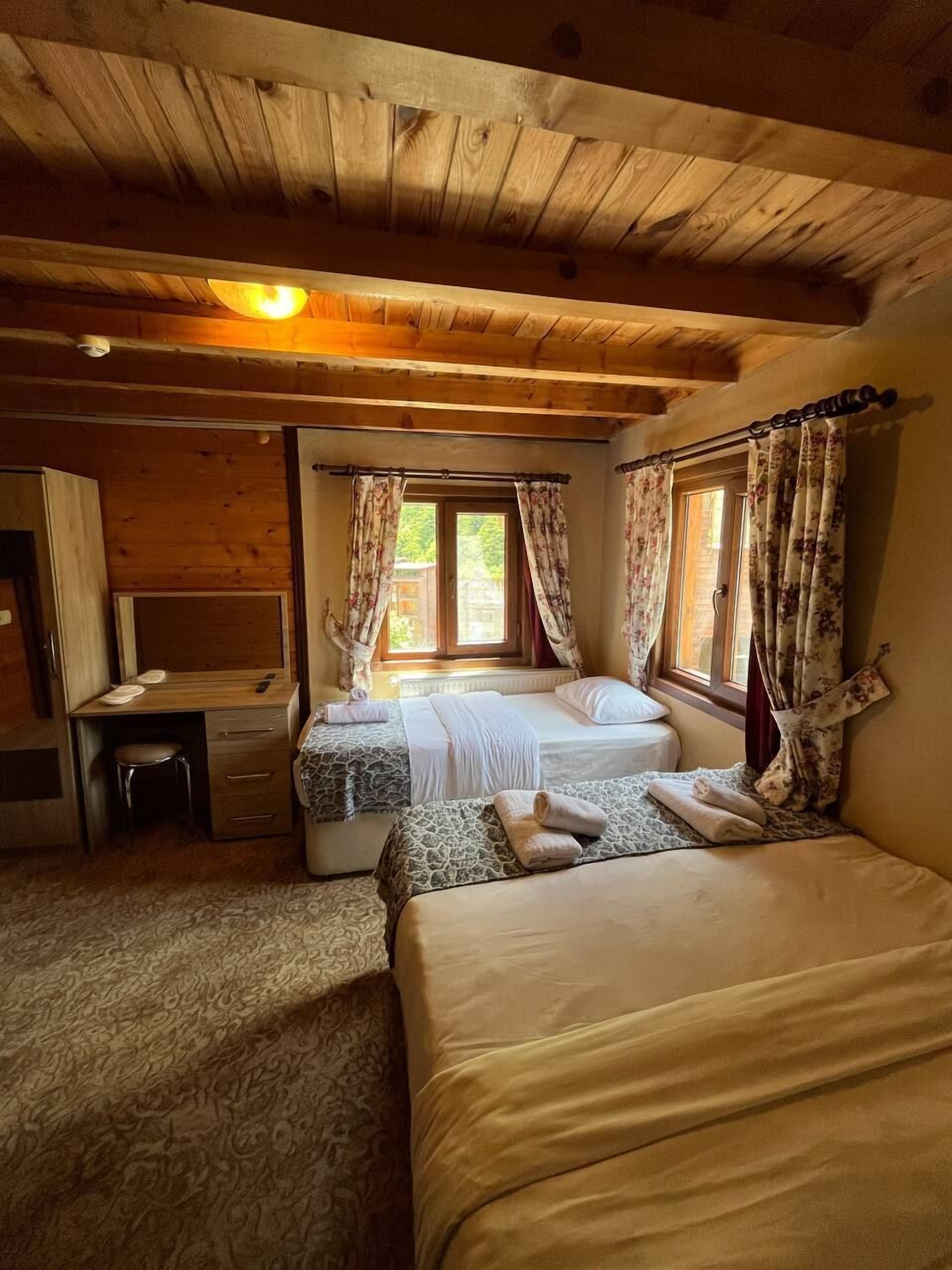 Um quarto acolhedor com duas camas, uma escrivaninha e janela com cortinas.