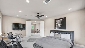 A bedroom with a large bed, a desk, a chair, a TV, and a ceiling fan. - Hill Country Hideaway (Austin)