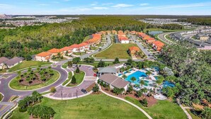 An aerial view of a residential area with a swimming pool, curved roads, and houses with red roofs.