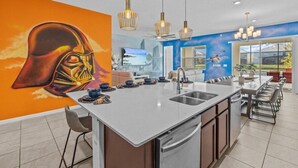 A modern kitchen with a central island, a large mural, and a dining area with chairs.