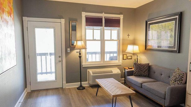 A living room with a gray sofa, a wooden coffee table, two floor lamps, a radiator, and a door with a window.