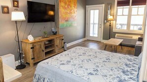 A bedroom with a large bed, a television, a painting, a desk, and a window.