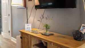 A modern living room with a flat-screen TV mounted on the wall, a wooden console table with a vase of flowers, and a lamp.