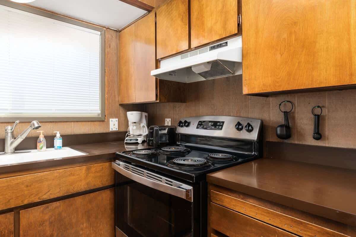 A kitchen with wooden cabinets, a stove, a coffee maker, and a window with blinds.