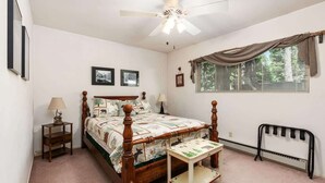 A bedroom with a wooden four-poster bed, a ceiling fan, a window with blinds, and a radiator.