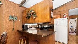 A kitchen with wooden cabinetry, a central island with stools, a refrigerator, and a decorative wall hanging.
