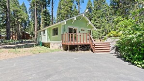 A small cabin with a porch, surrounded by tall trees.