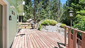 A wooden deck leading to a building with a green exterior, surrounded by trees and a rock.
