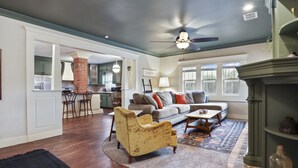 A spacious living area with a fireplace, a dining area with bar stools, and a kitchen with green cabinets.