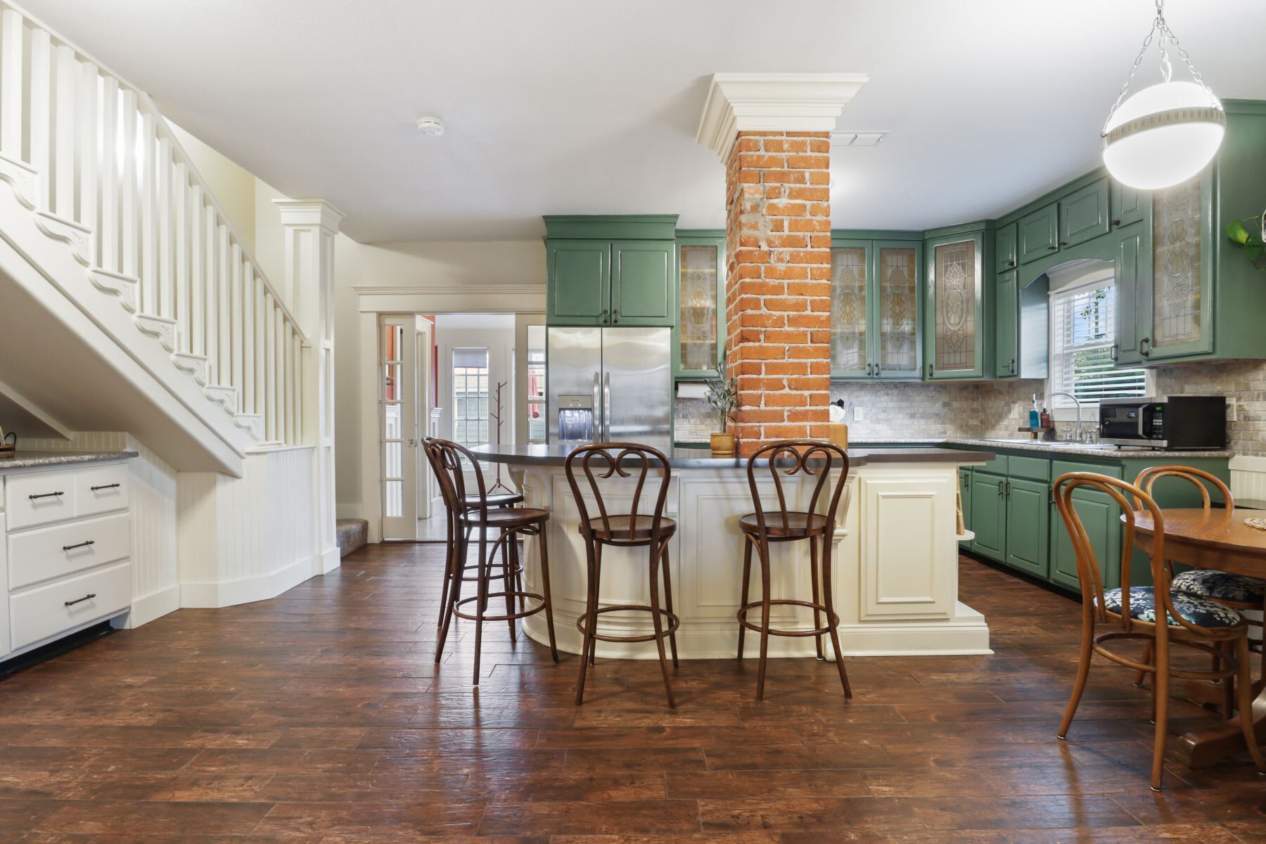 A kitchen with green cabinets, a brick column, and a wooden floor.