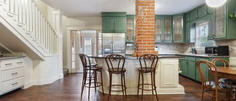A kitchen with green cabinets, a brick column, and a wooden floor.