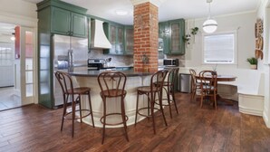 A kitchen with green cabinets, a brick column, and a central island with bar stools.