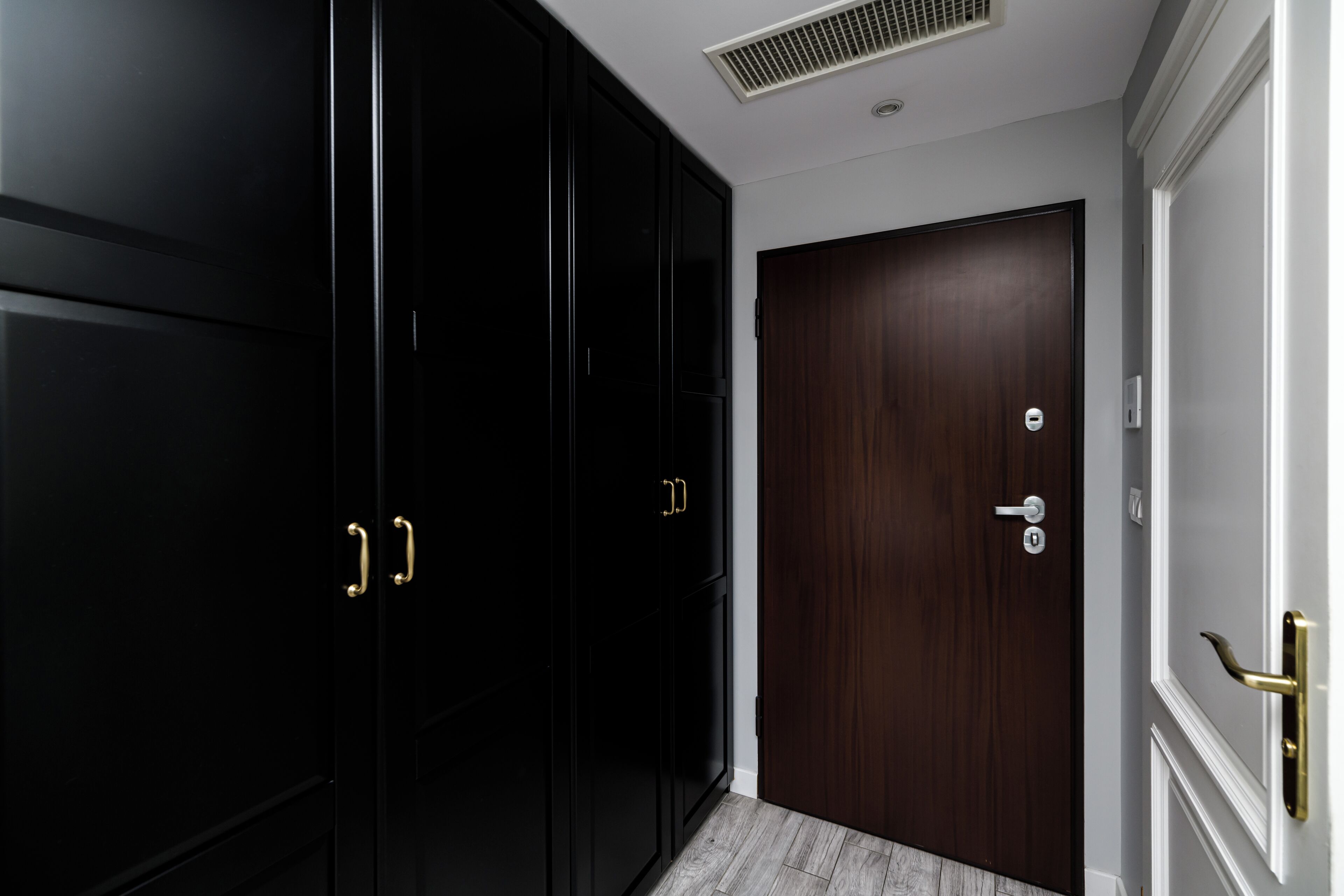 Un couloir avec des meubles noirs, une porte en bois et un mur blanc.