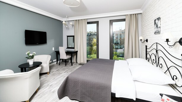 Ett modernt hotellrum med en säng, ett skrivbord, en stol, en TV och utsikt över staden.