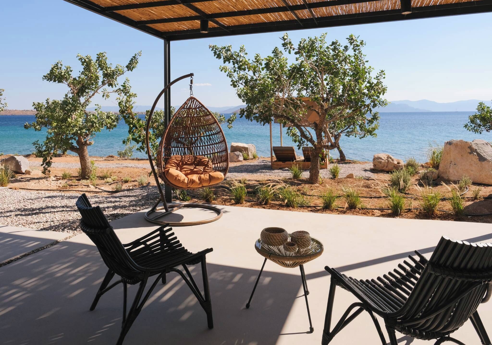 An outdoor seating area with a hanging chair, two lounge chairs, and a small table with woven baskets.