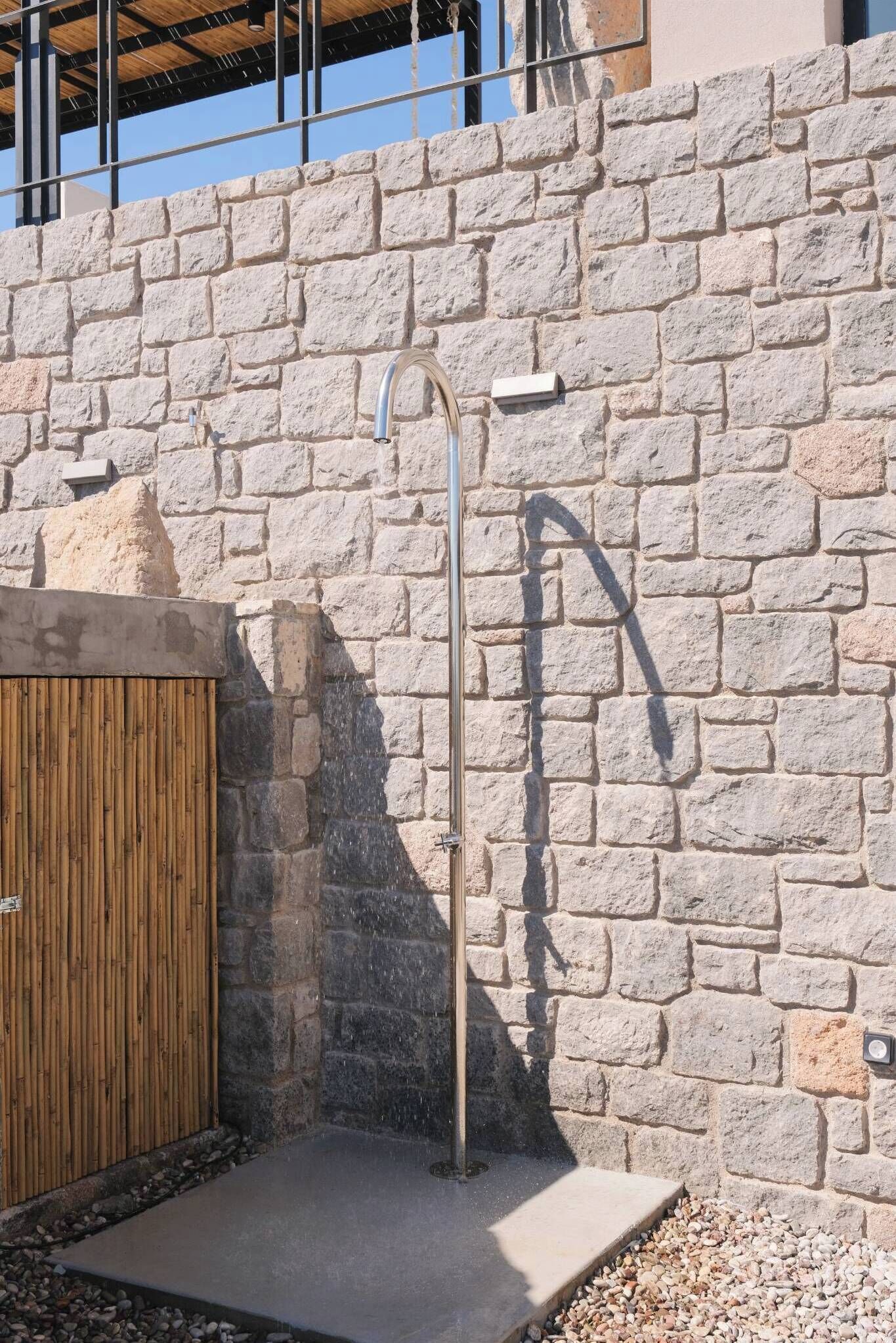 A stone wall with a metal outdoor shower and a wooden door.