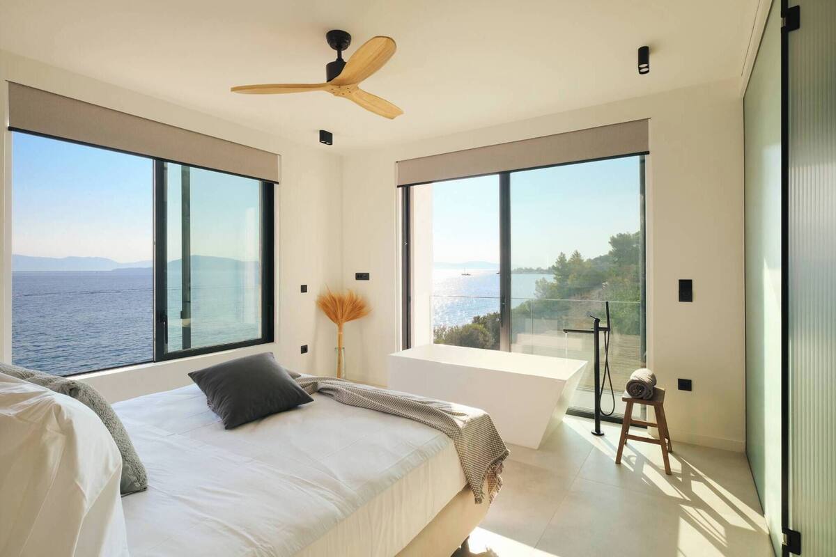Ein modernes Schlafzimmer mit einem großen Bett, einem Deckenventilator und Meerblick.