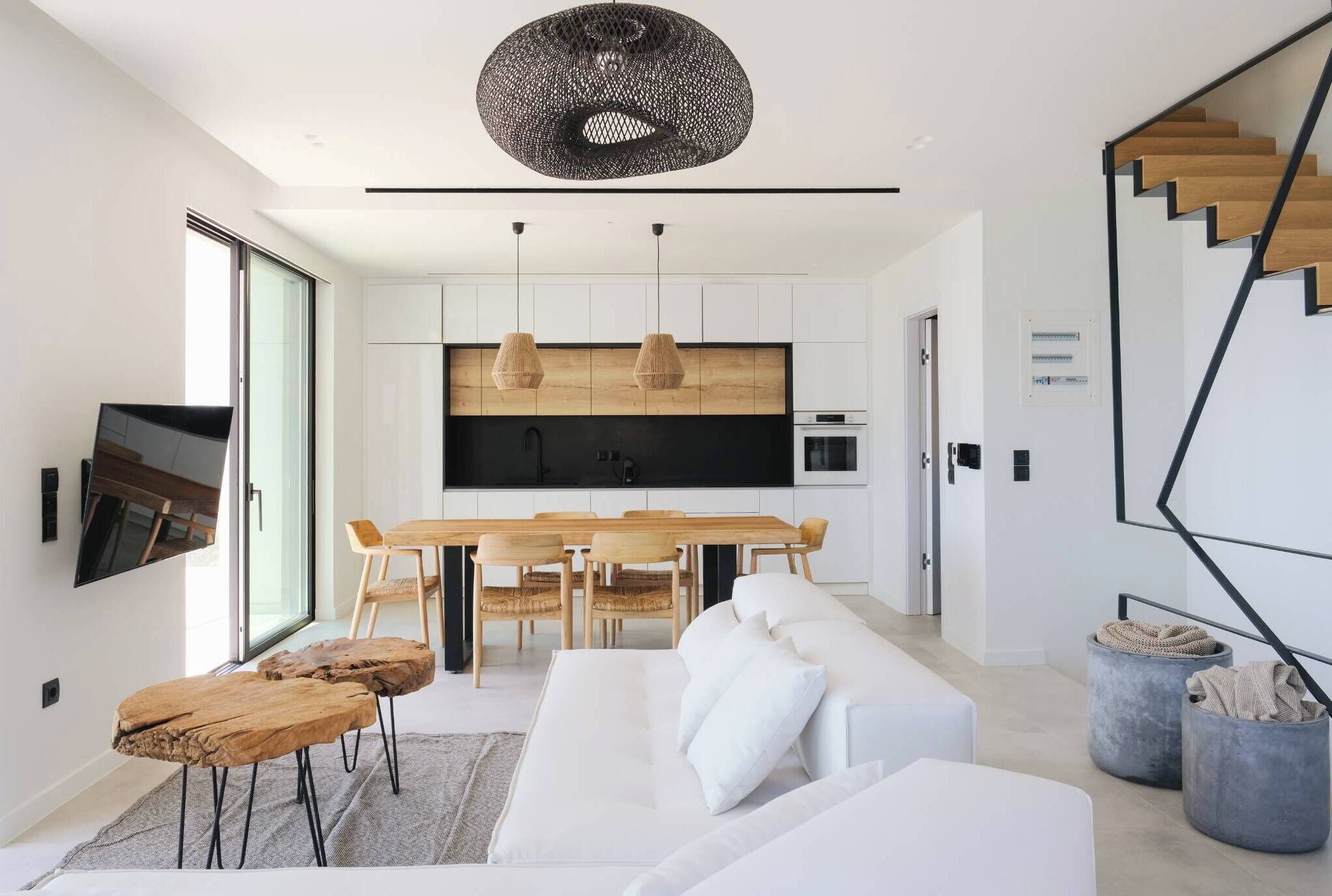 A modern kitchen with a black countertop, wooden dining table, and hanging pendant lights.