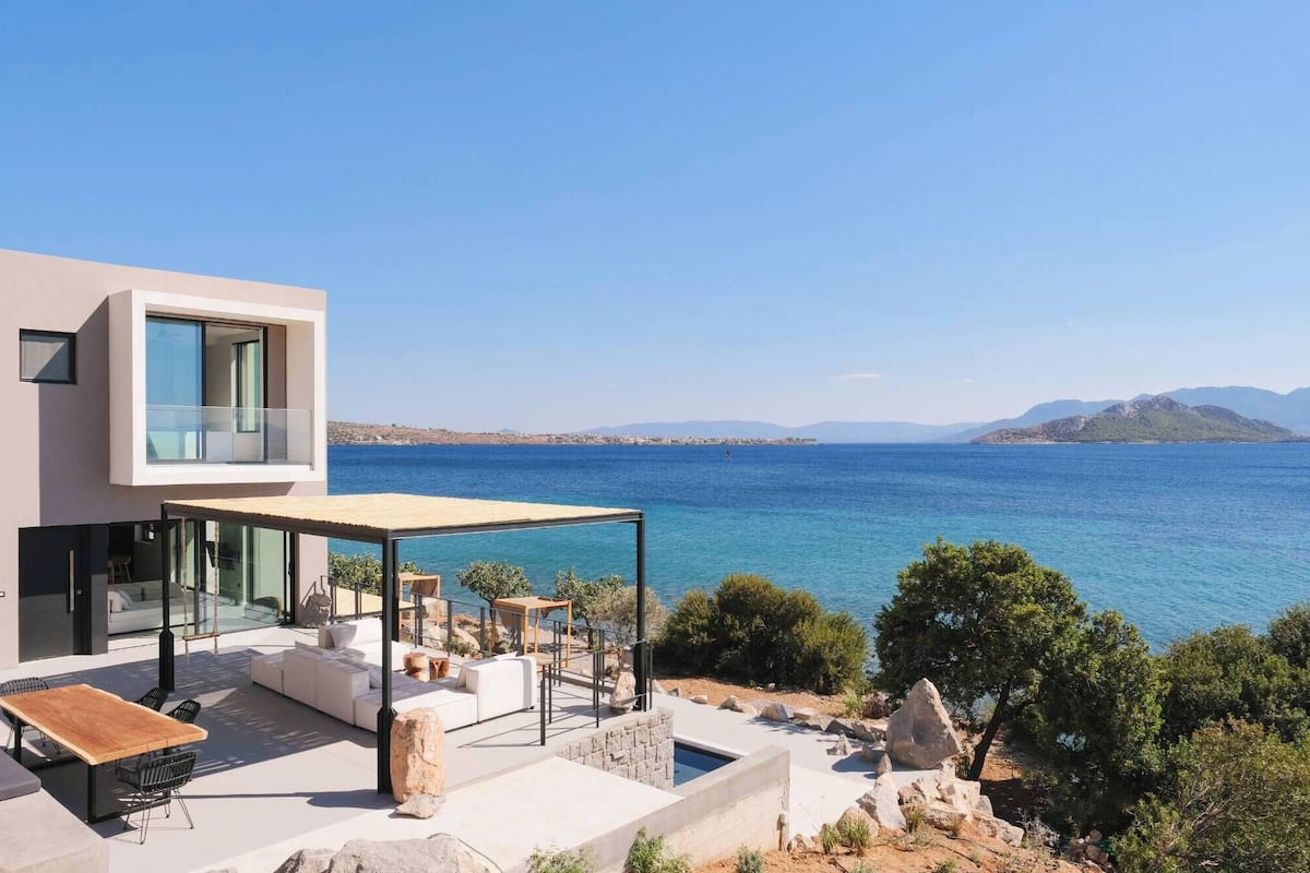 Ein moderner Außenbereich mit Pool, mit Blick auf das klare, blaue Meer und entfernte Berge.