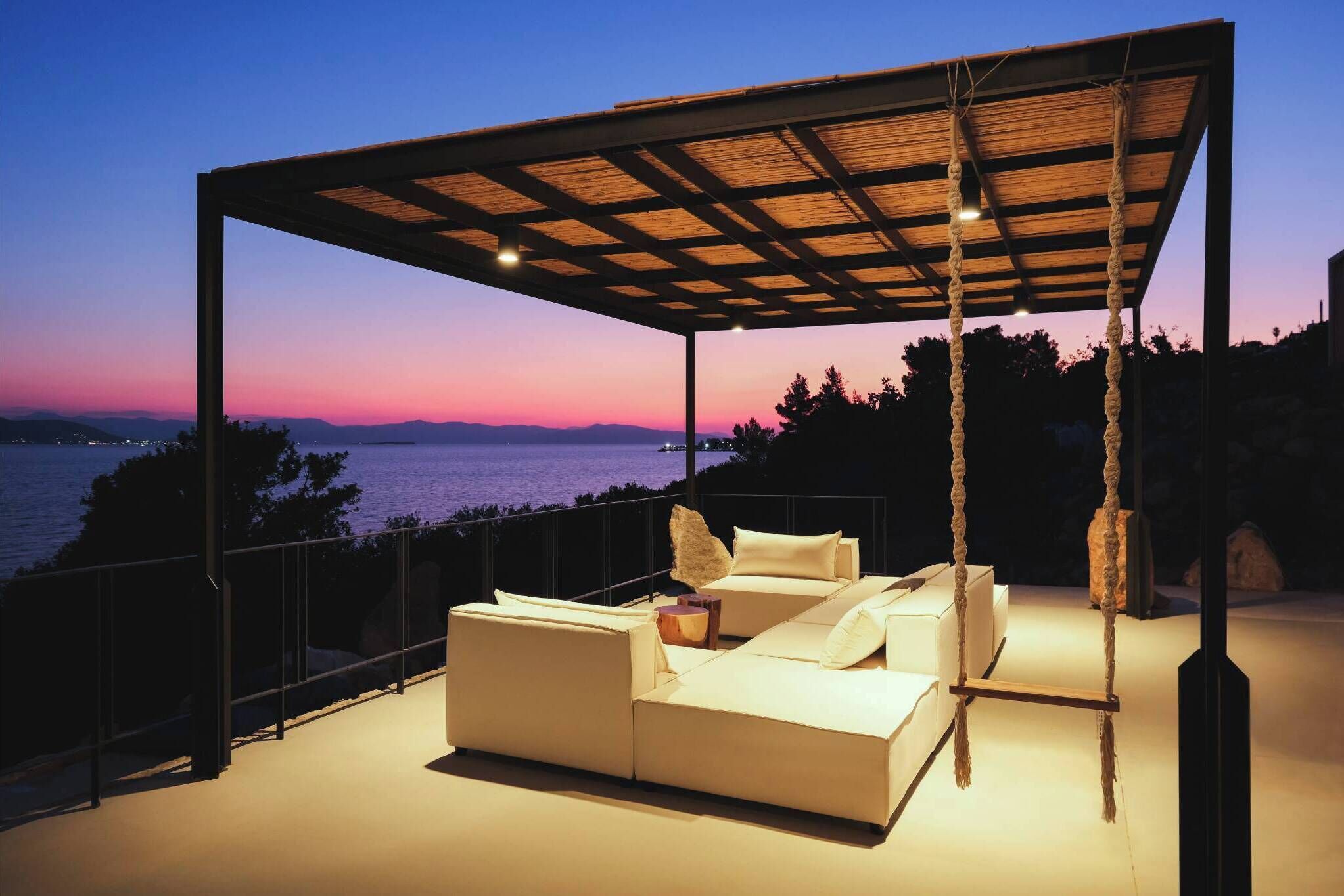 Un espace extérieur abrité, aménagé avec des sièges, et offrant une vue sur la mer au crépuscule.