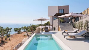 A modern poolside area with a clear view of the sea, lounge chairs, and umbrellas. - Floating Cubes Villas Aegina (Aegina)