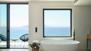A modern bathroom with a large bathtub, a small stool, and a view of the sea through a large window. - Floating Cubes Villas Aegina (Aegina)