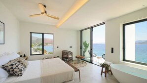 A modern bedroom with a large bed, a ceiling fan, a view of the sea, and a bathtub. - Floating Cubes Villas Aegina (Aegina)