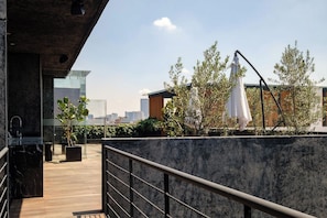 A rooftop terrace with a wooden deck, a concrete wall, and a city skyline in the background.