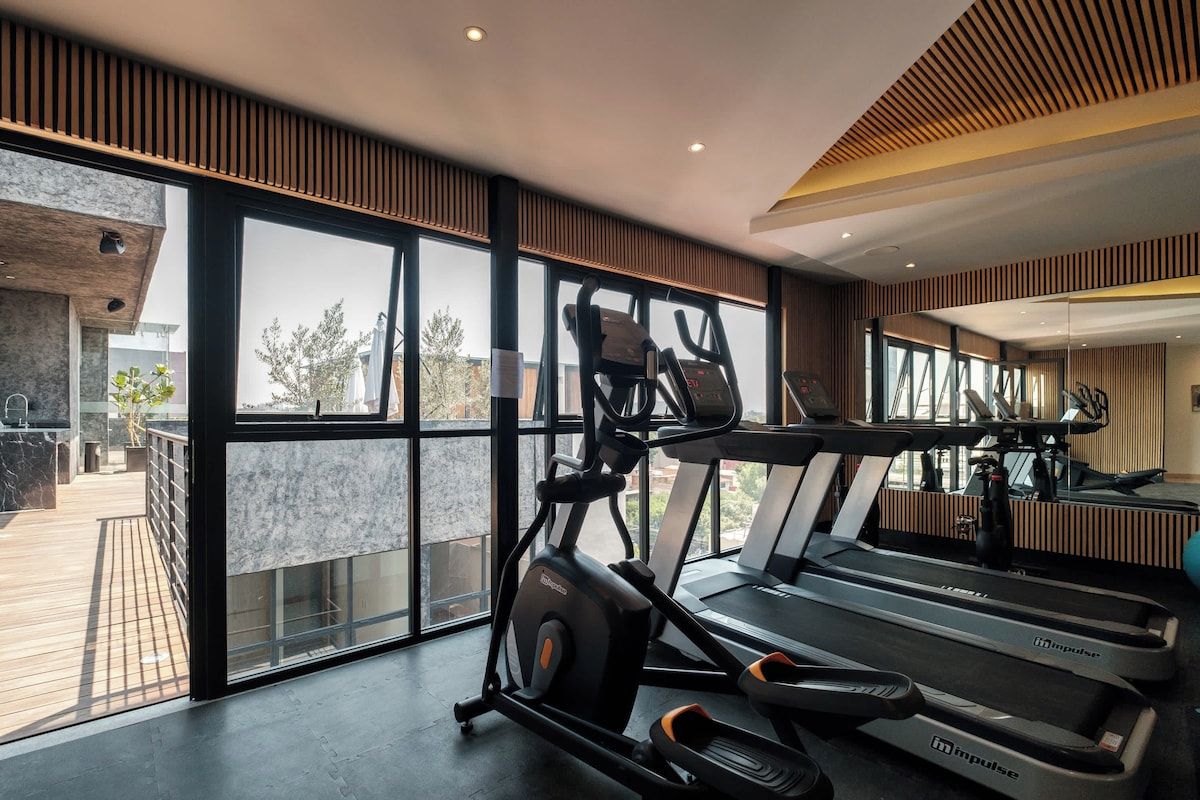 A gym with exercise equipment, large windows, and a view of the outdoors.
