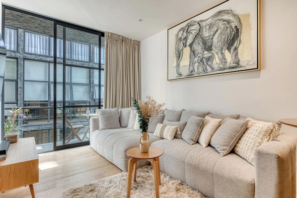 Ein modernes Wohnzimmer mit großem Fenster, einer Couch, einem kleinen Tisch mit einer Vase und einem gerahmten Kunstwerk an der Wand.