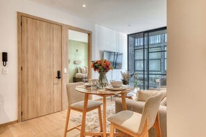 A modern dining area with a wooden table and chairs, a vase with flowers, and a large window with a view.