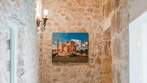 A stone wall with a framed picture of a historic building, a wall-mounted light fixture, and a door. - Villa Oliva Sleeps 8 With Gym (Xaghra)